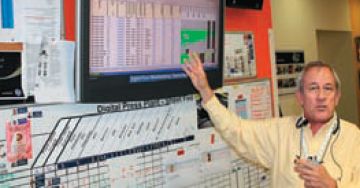 Директор завода объясняет, как формируется производственный план. Он отображается на большом экране, ниже рабочие отмечают выполнение каждого производственного этапа на пластиковой доске